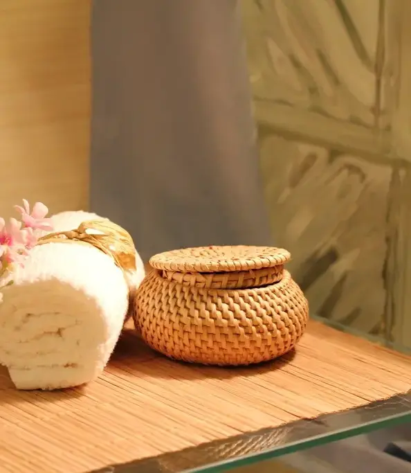 Toalla enrollada, flores y una cesta de mimbre sobre una bandeja de madera