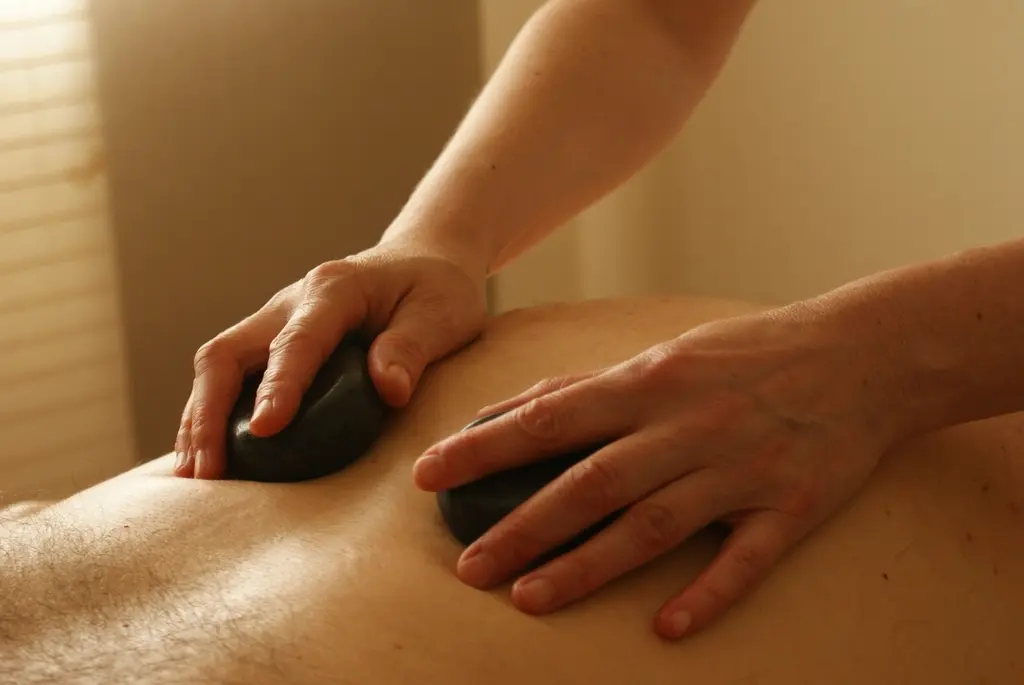 Dos manos con piedras de masaje sobre una espalda