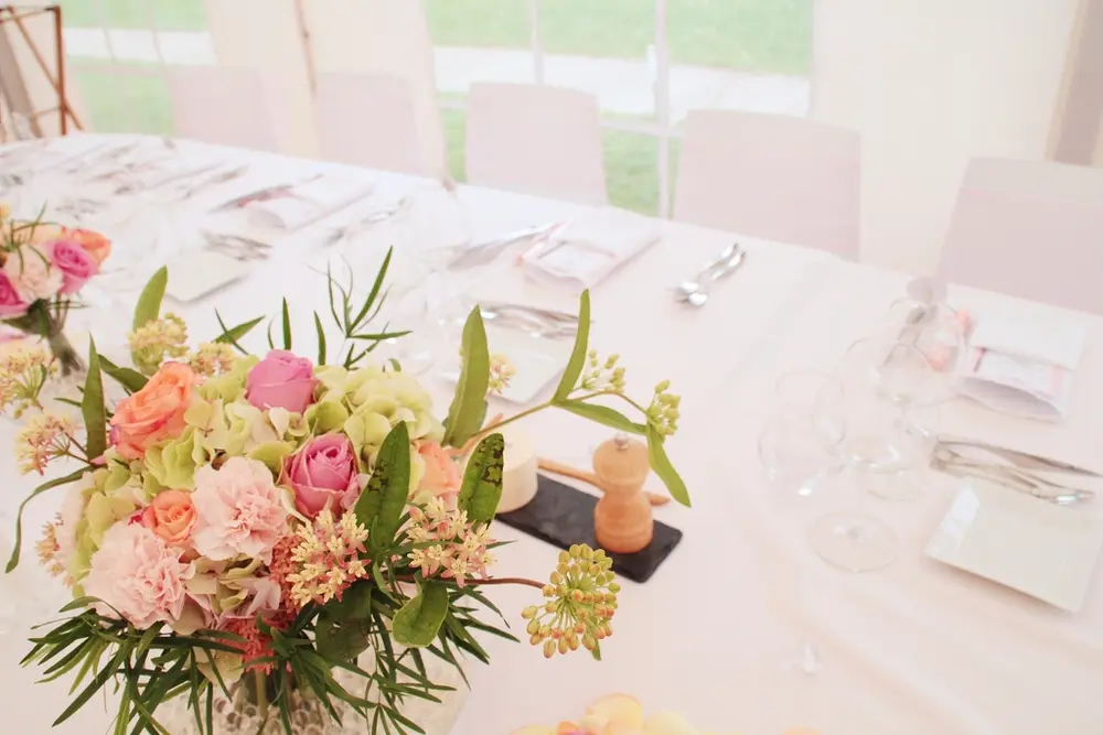 Centro bajo de rosas y claveles en una mesa de banquete vestida de blanco.