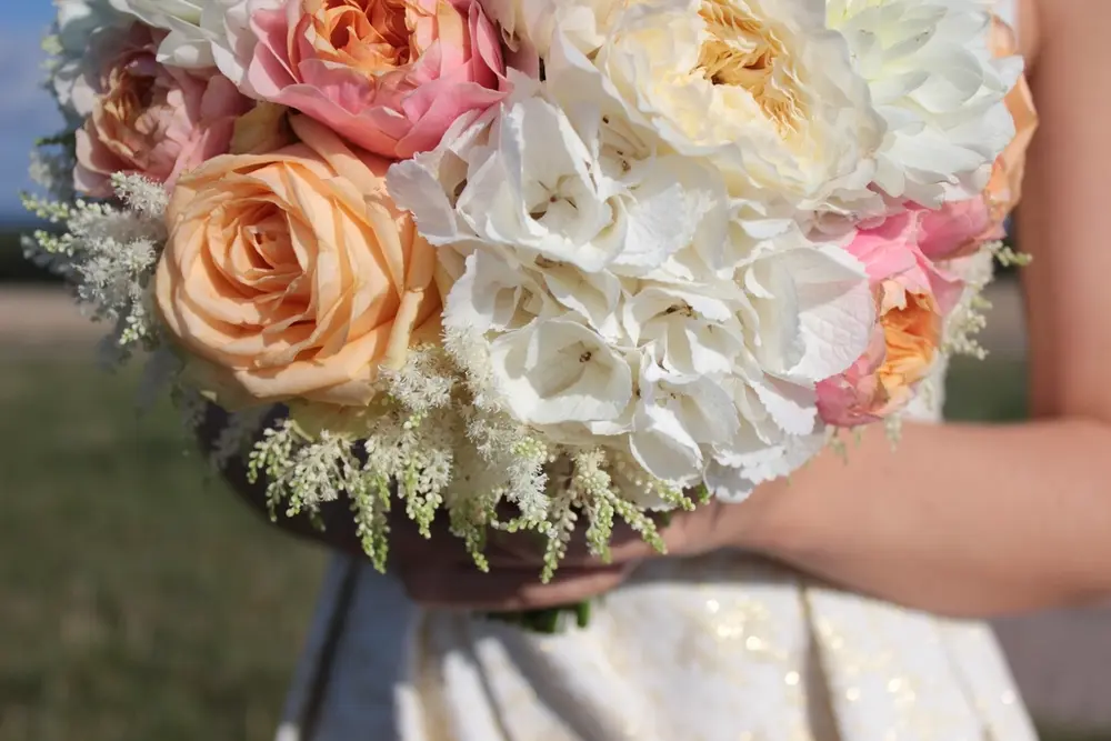 Novia con un ramo de rosas color melocotón e hortensias blancas.