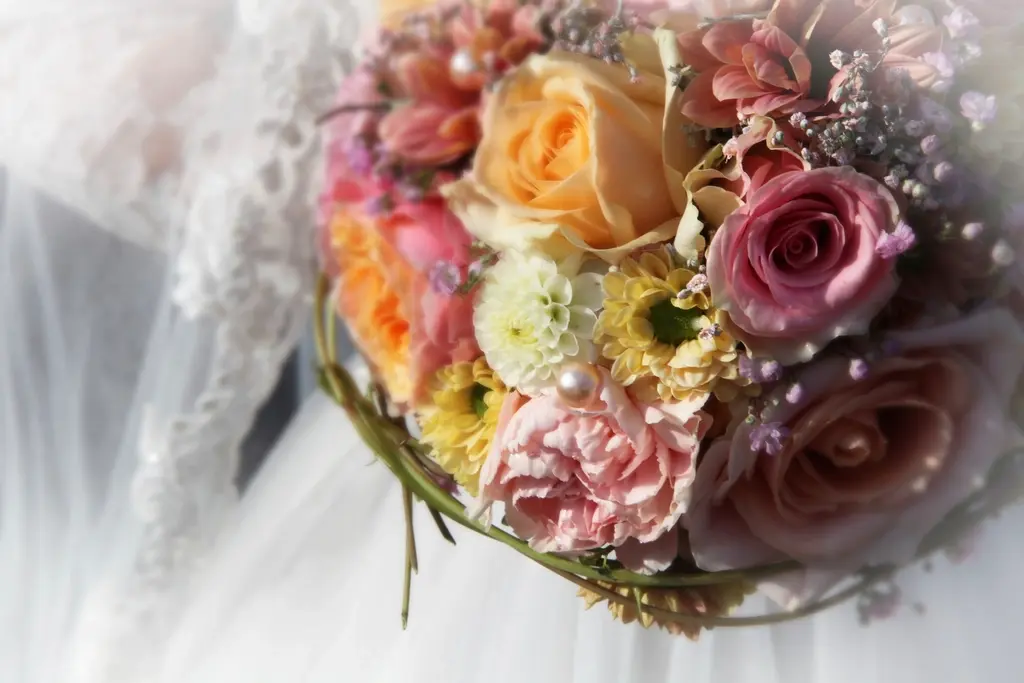 Ramo de novia redondo de rosas y claveles con un velo blanco detrás.