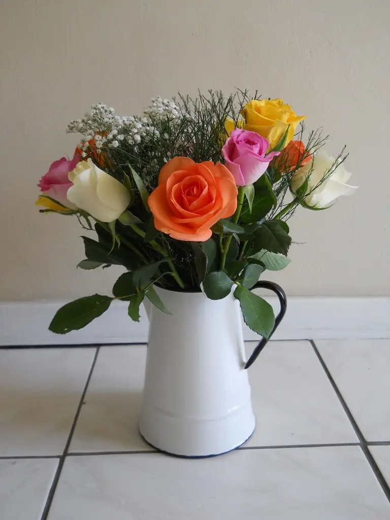 Ramo de rosas naranjas, amarillas, rosas y blancas en una jarra de porcelana blanca.