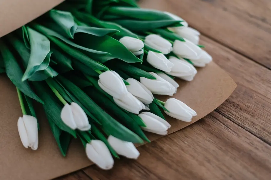 Tulipanes blancos atados sobre papel de estraza y una mesa de madera.