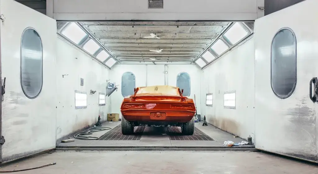 Cabina de pintura blanca e iluminada, con un coche rojo recién pintado dentro