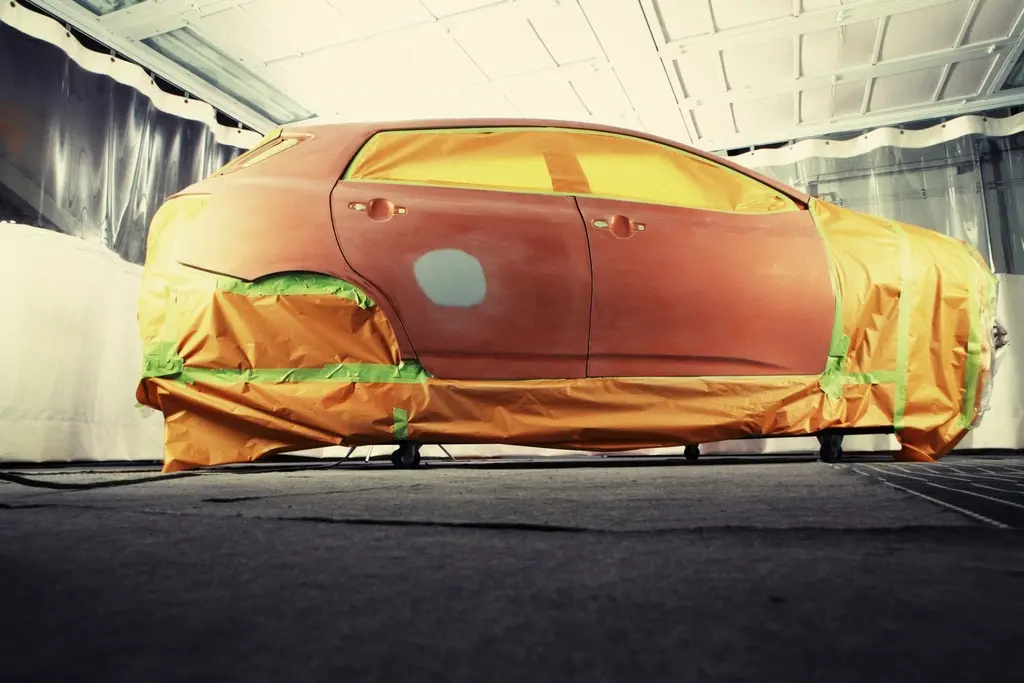 Coche cubierto con papel y cinta de enmascarar dentro de la cabina de pintura, con una puerta lijada lista para pintar