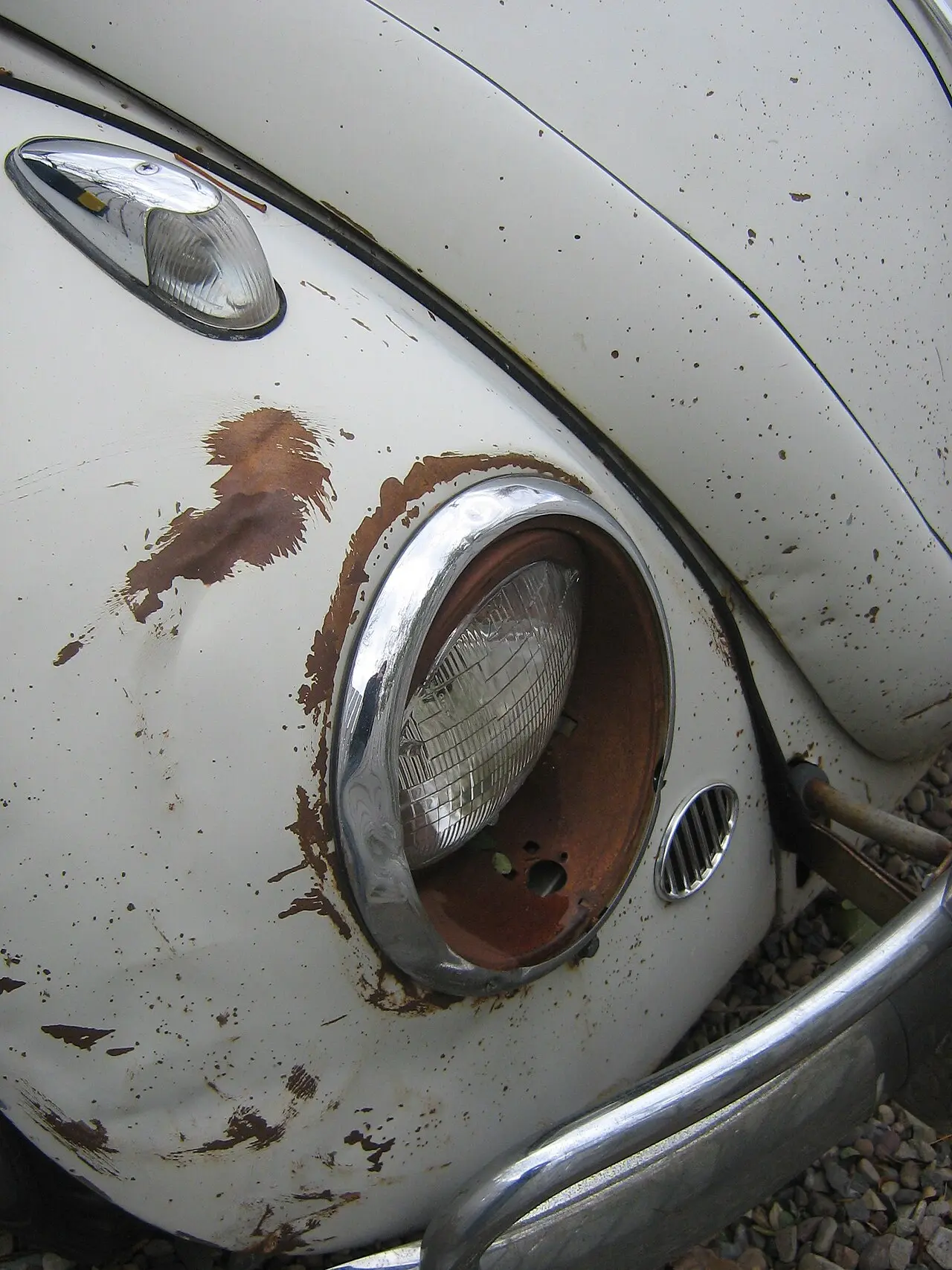 Faro redondo de un coche clásico blanco con óxido alrededor del aro