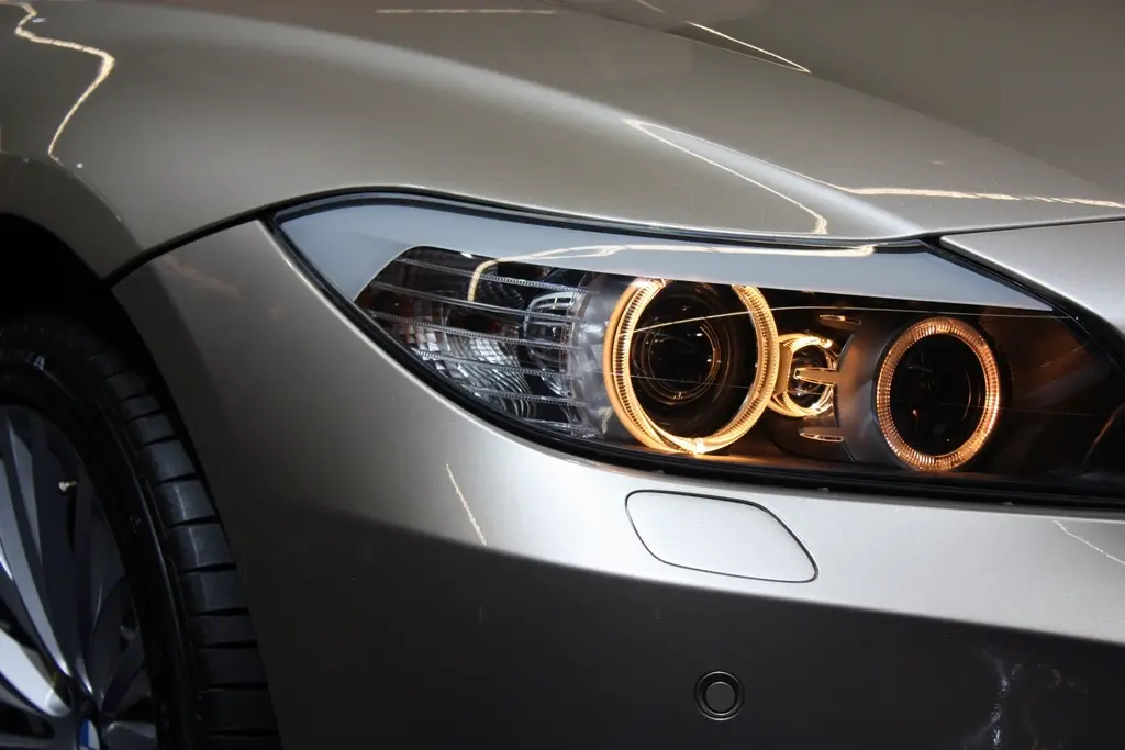 Frontal de un coche gris recién pintado, con la carrocería brillante y el faro nuevo encendido