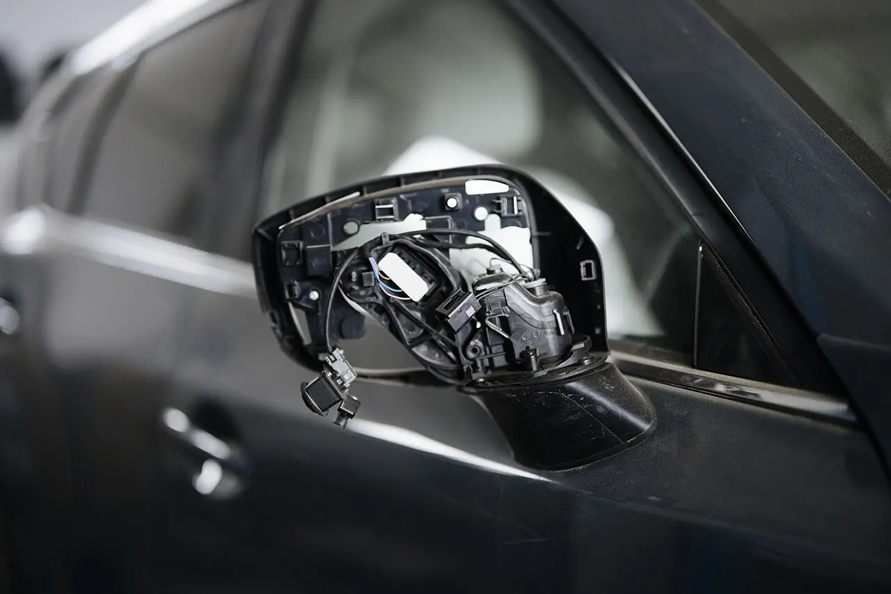 Retrovisor de un coche oscuro roto, con los cables y el soporte a la vista