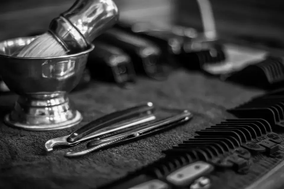 Brocha de afeitar en su cuenco, navajas y peines sobre una toalla, en blanco y negro