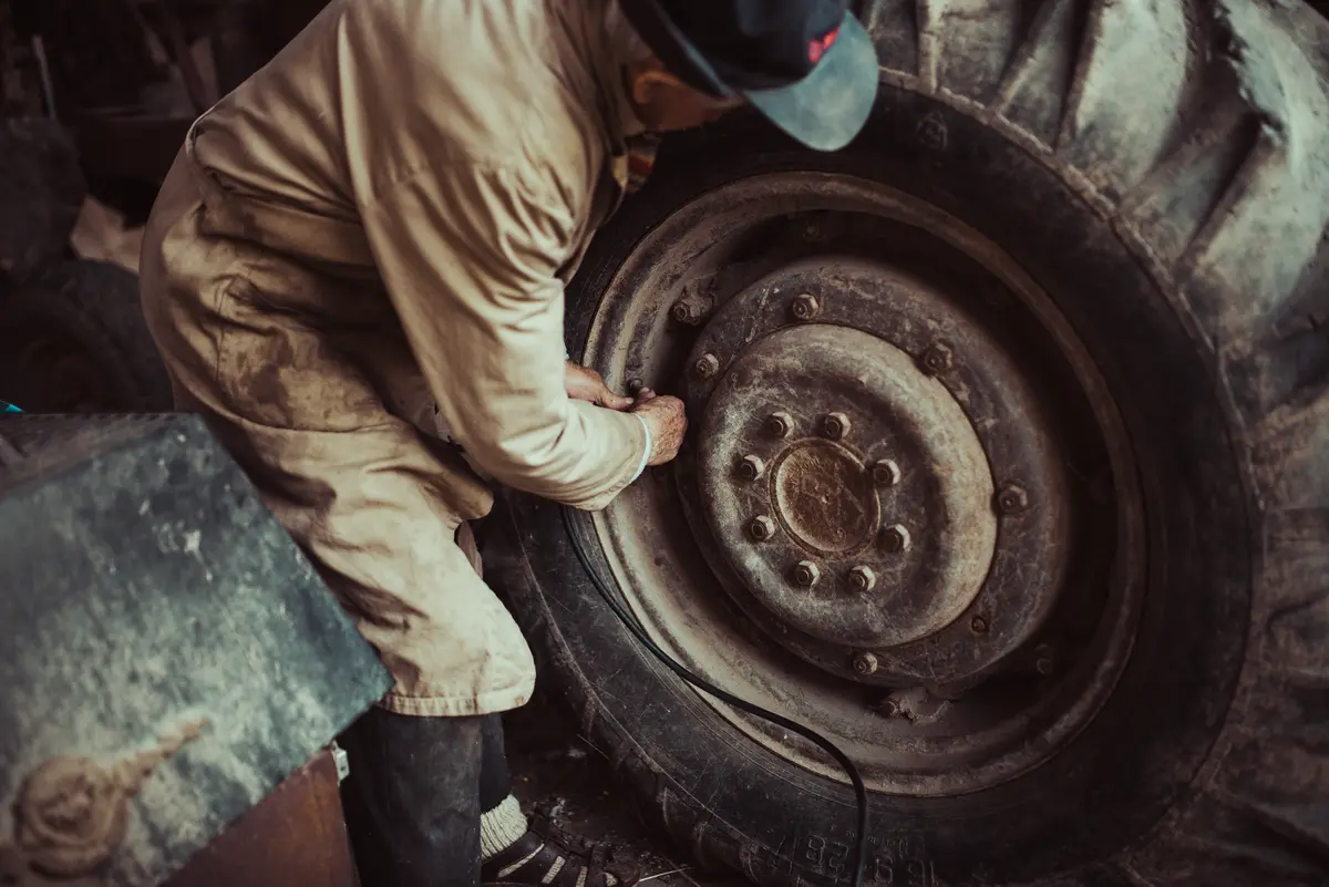 Un mecánico con mono de trabajo aprieta las tuercas de la rueda de un tractor en el taller