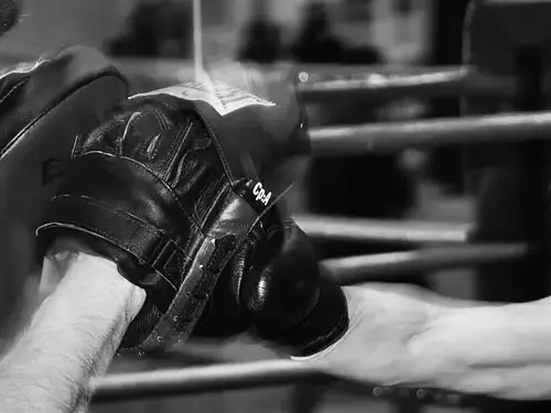 Guante de boxeo golpeando las manoplas del entrenador junto a las cuerdas del ring