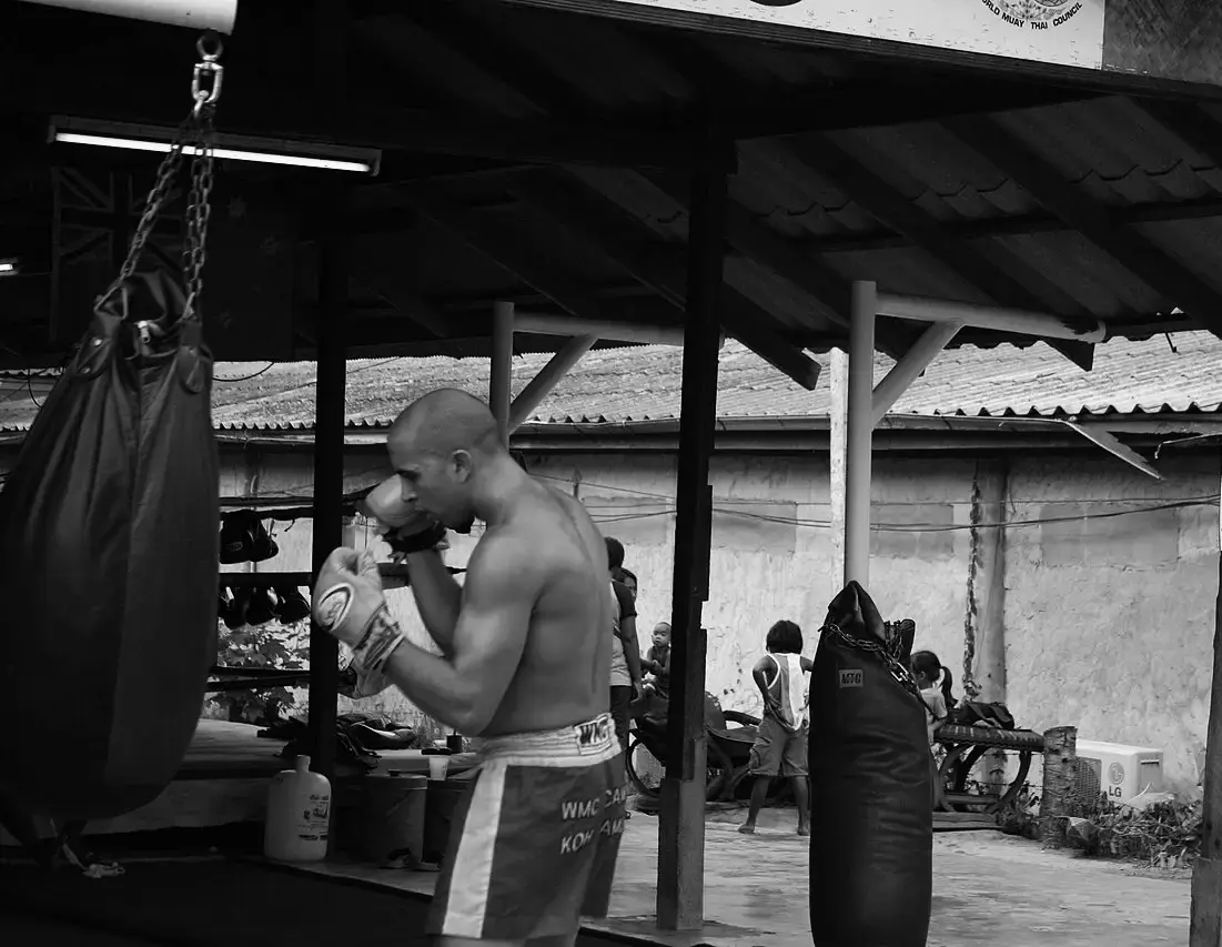 Hombre golpeando un saco con guantes en un gimnasio abierto, con más sacos colgados
