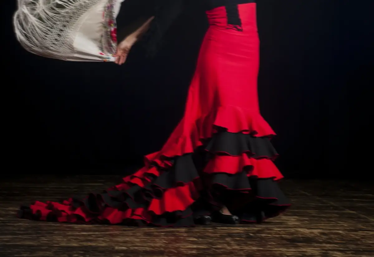 Falda roja de flamenco con volantes negros arrastrando por el suelo del escenario, en movimiento