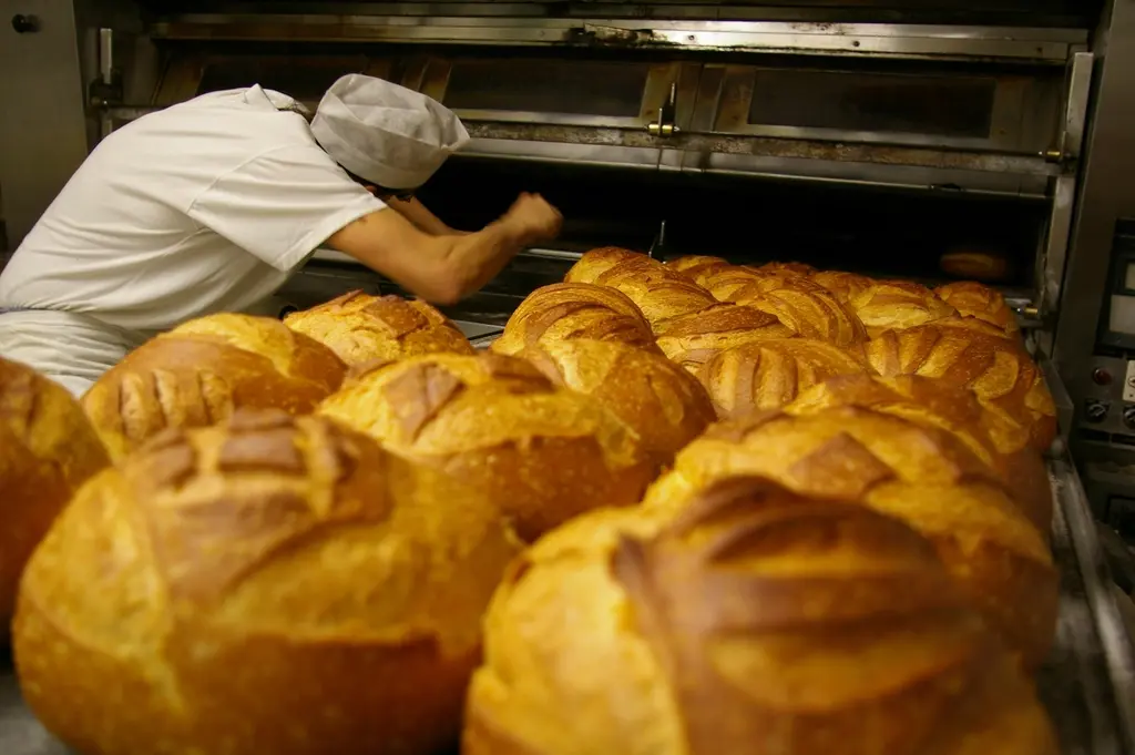 Hogazas recién sacadas del horno de leña, con la corteza tostada y el hornero al fondo