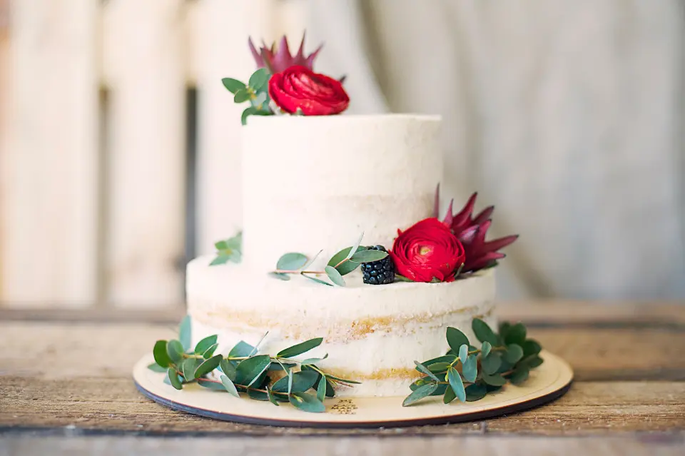 Tarta de dos pisos con nata y flores sobre una tabla de madera