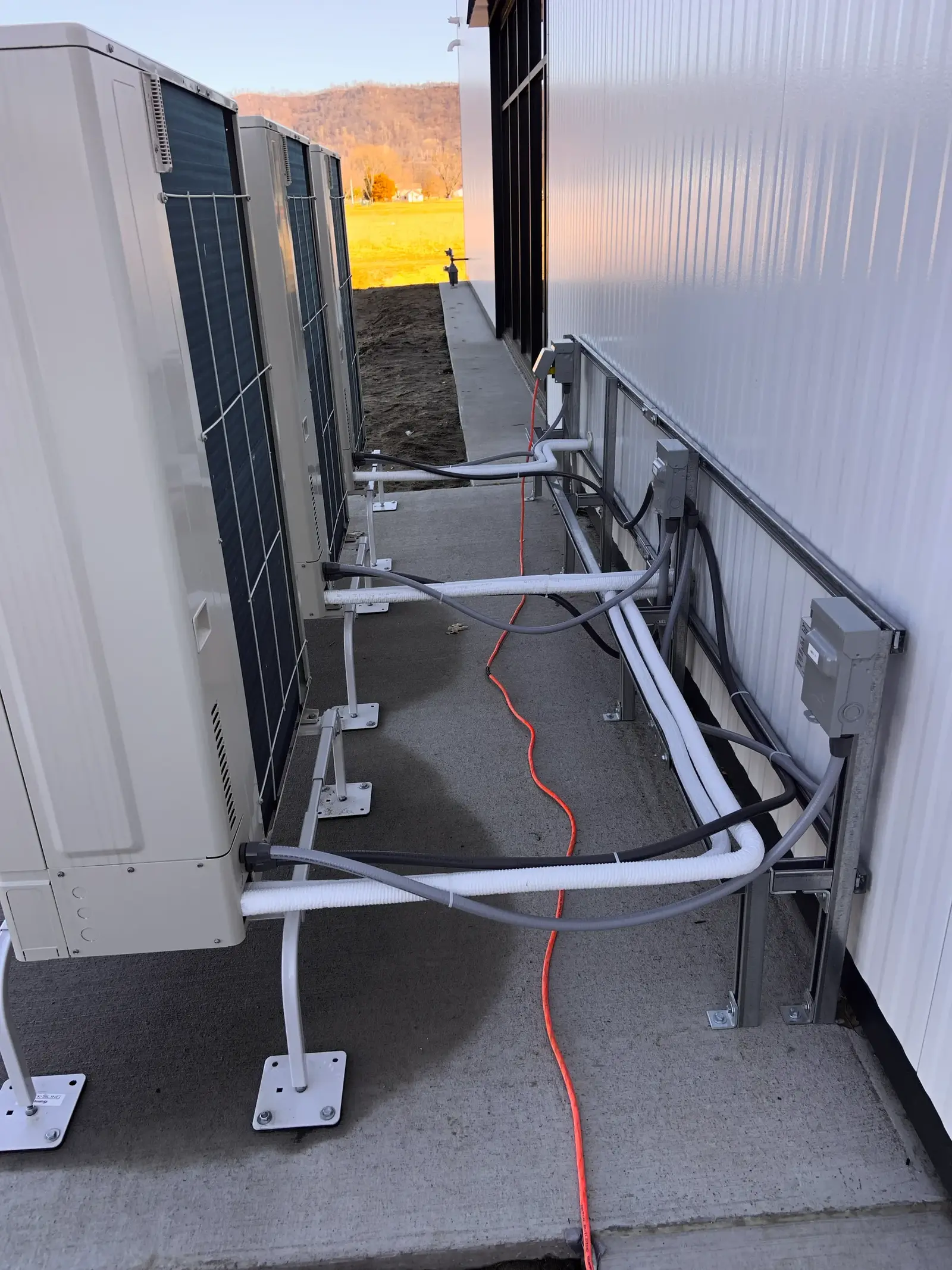 Tres unidades exteriores de bomba de calor alineadas sobre soportes junto a la pared de una nave