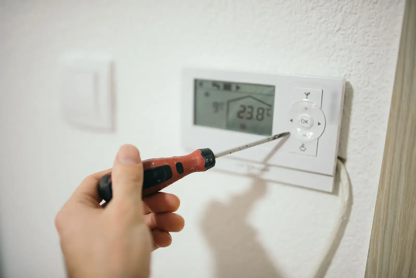 Un técnico ajusta con un destornillador el termostato de una pared