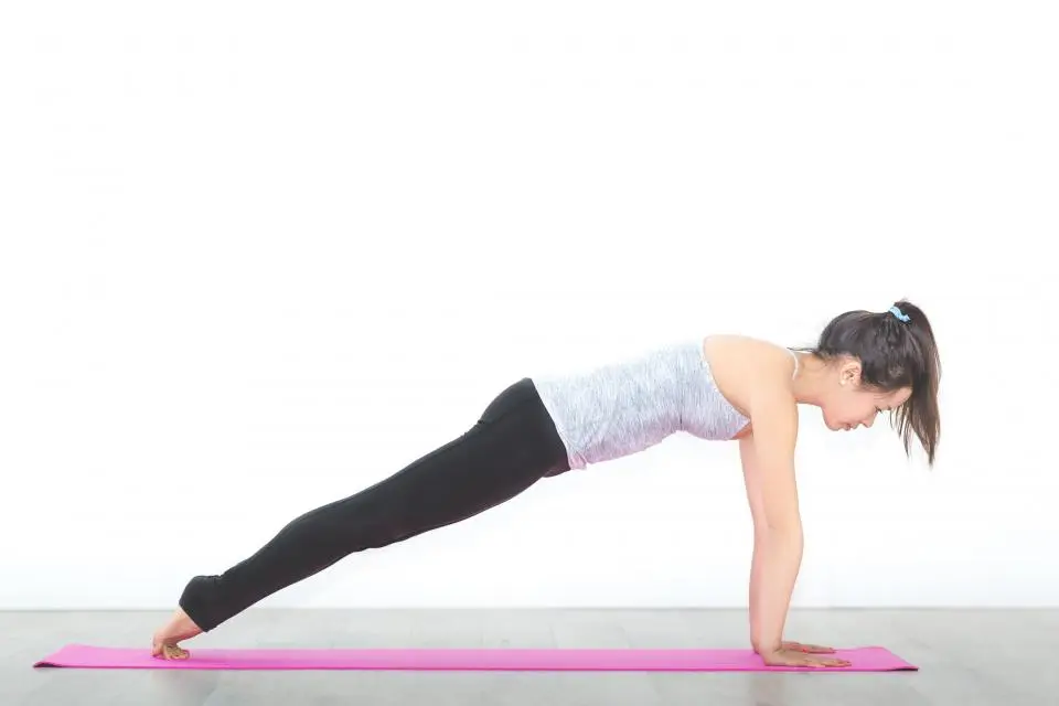 Una mujer haciendo una plancha sobre una esterilla en una sala blanca.