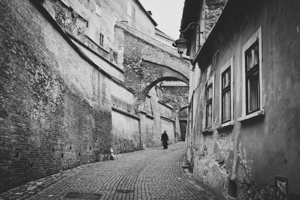 Calle empedrada de casco viejo con un arco, en blanco y negro