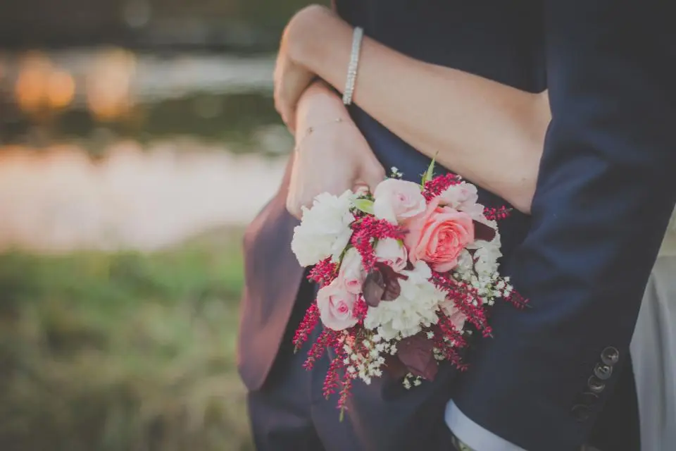 Ella abraza al novio con un ramo de rosas a su espalda