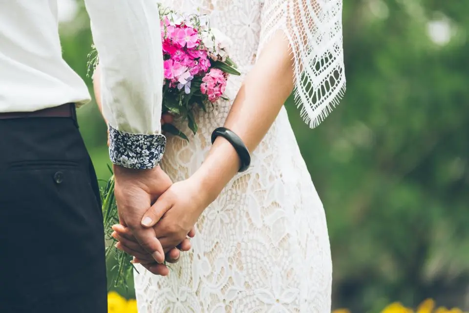 Los novios se cogen de la mano junto a un ramo de flores rosas
