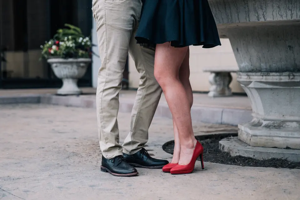 Las piernas de la pareja, muy juntos, ella con zapatos rojos en una plaza