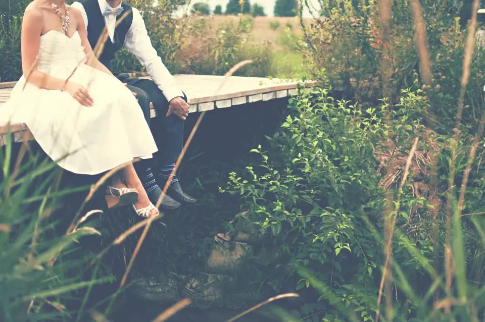 La pareja sentada en un puente de madera entre la hierba alta