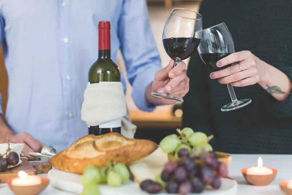 Dos copas de tinto brindan sobre una mesa con pan y uvas