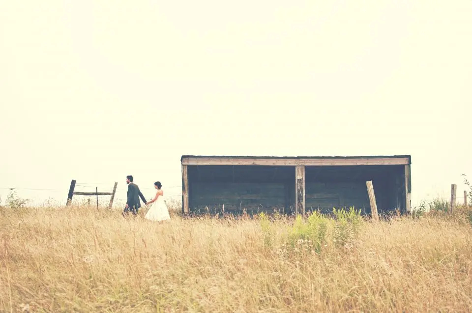Los novios caminan a lo lejos por un campo de hierba seca junto a un pajar