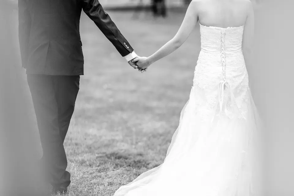 Los novios de espaldas, cogidos de la mano sobre la hierba, en blanco y negro