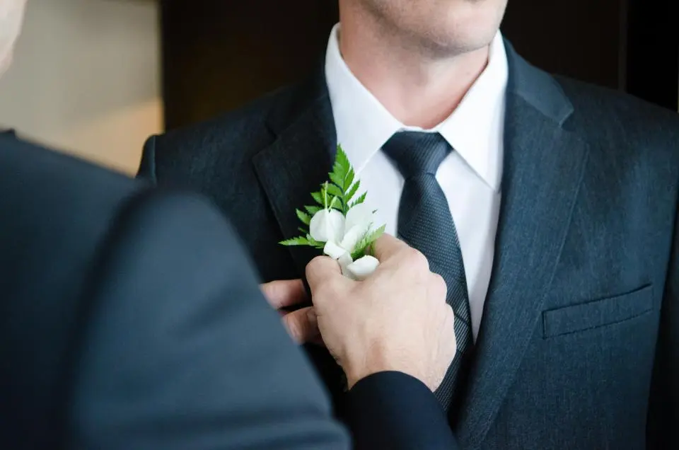 Una mano coloca el prendido de flores blancas en la solapa del novio