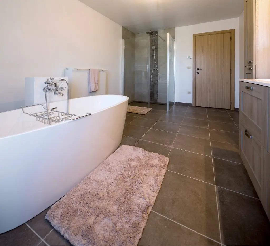 Baño con bañera exenta blanca, suelo de baldosa gris y ducha al fondo