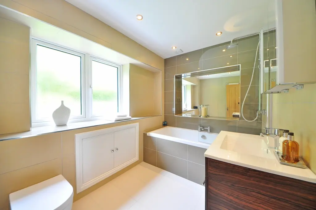 Baño beis con bañera bajo la ventana, lavabo con mueble de madera oscura y espejo