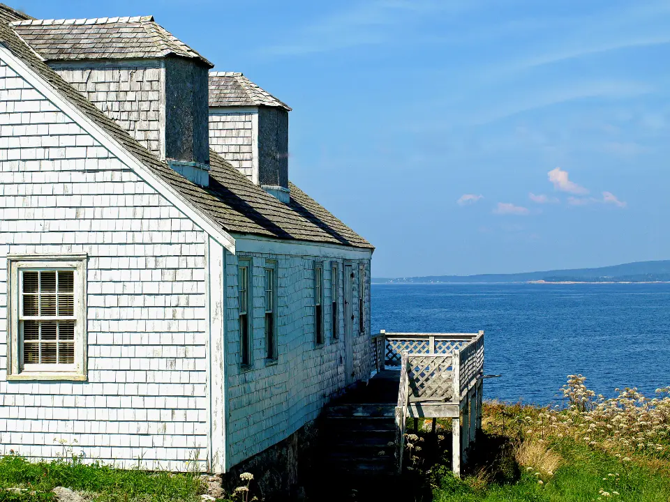 Fachada de tablilla blanca de una casa junto al mar, con cielo azul