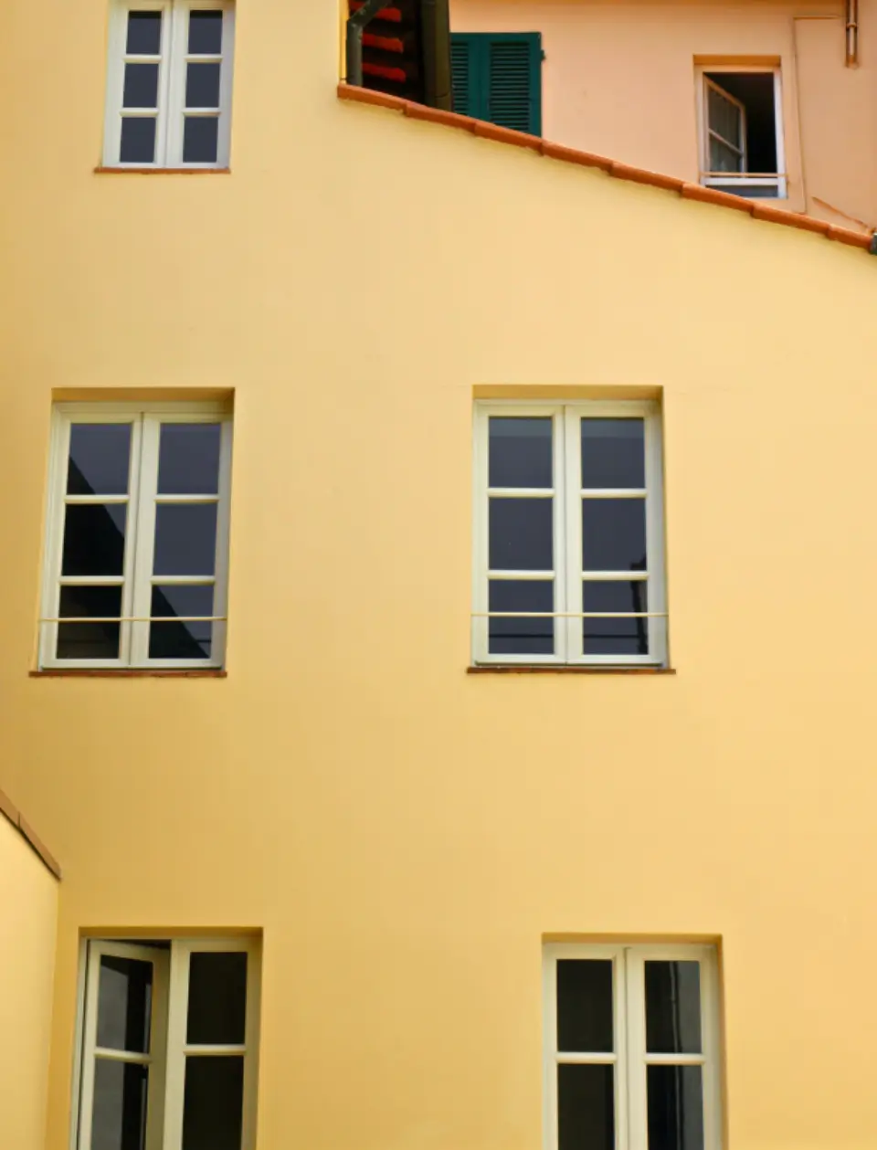 Fachada pintada en ocre claro con ventanas blancas