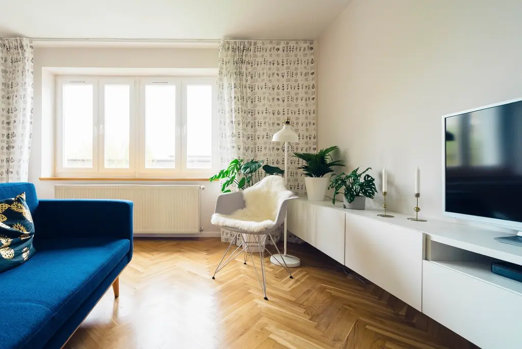 Salón recién pintado de blanco, con ventanal, sofá azul y suelo de madera en espiga