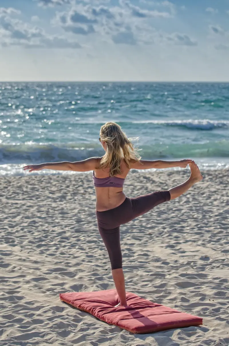 Una mujer en una postura de equilibrio en la orilla, vista de espaldas.