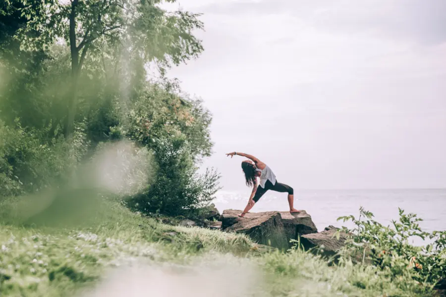 Una mujer estirando al aire libre junto al mar, de lejos.