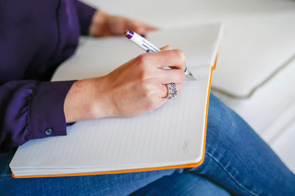 Manos escribiendo en un cuaderno abierto apoyado en las rodillas.