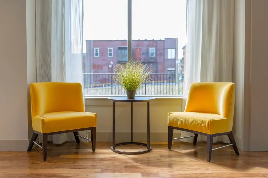 Dos sillones amarillos y una mesa baja con una planta, junto a un ventanal con cortinas claras.