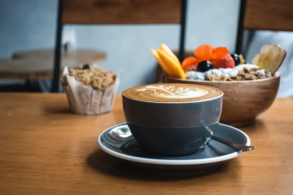 Capuchino, bol de granola y magdalena en una mesa junto a la ventana