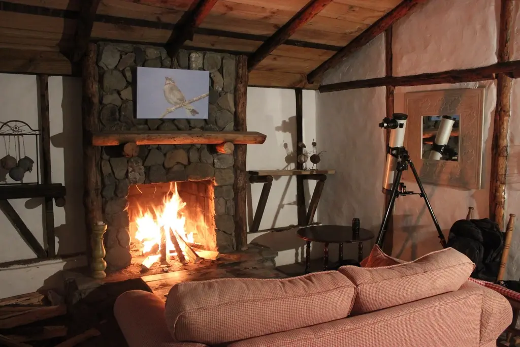 Salón de El Horno con la chimenea encendida, vigas de madera y sofá.