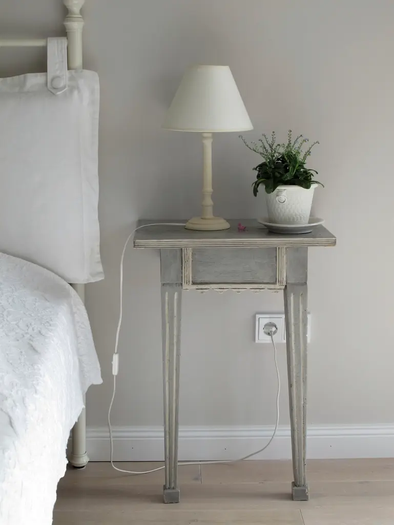 Mesilla con lámpara y una maceta junto a la cama del dormitorio principal.
