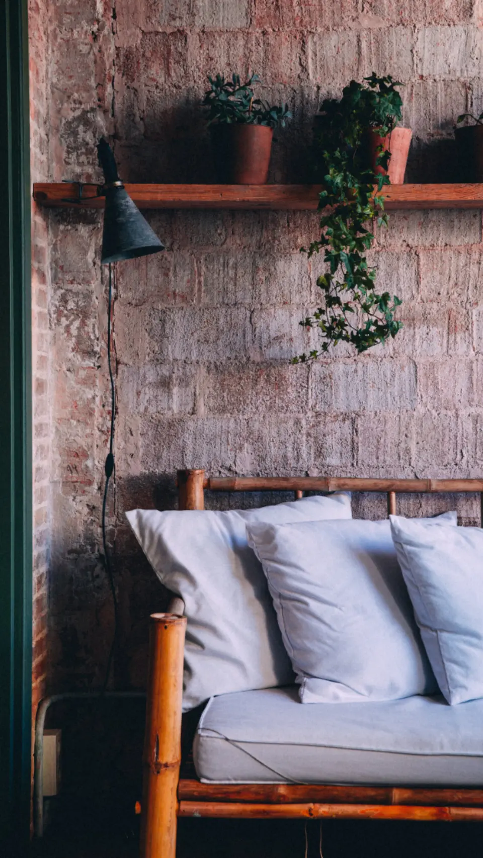 Sofá con cojines blancos bajo una pared de ladrillo con plantas colgantes.