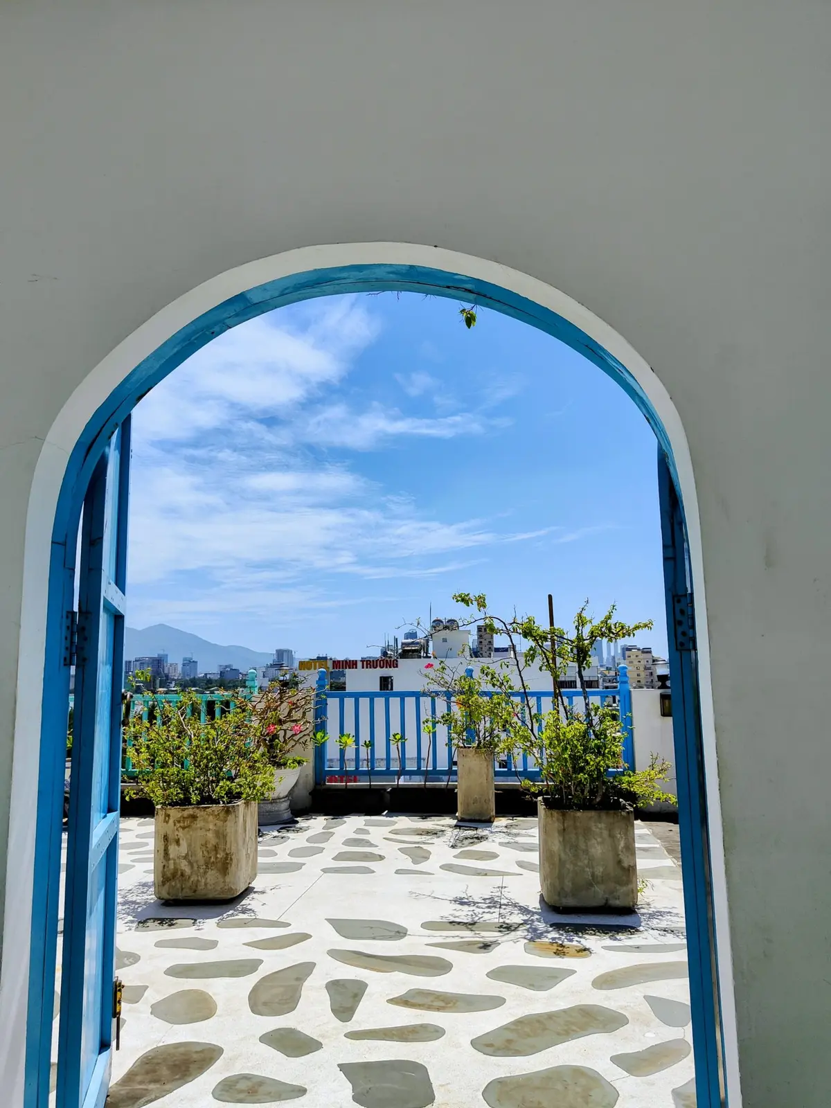 Puerta en arco pintada de añil que se abre a la terraza encalada, con macetas y la sierra al fondo.