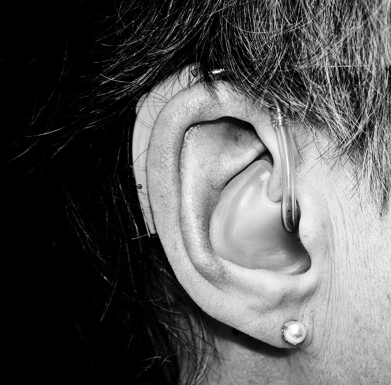 Oreja con un audífono pequeño detrás, en blanco y negro