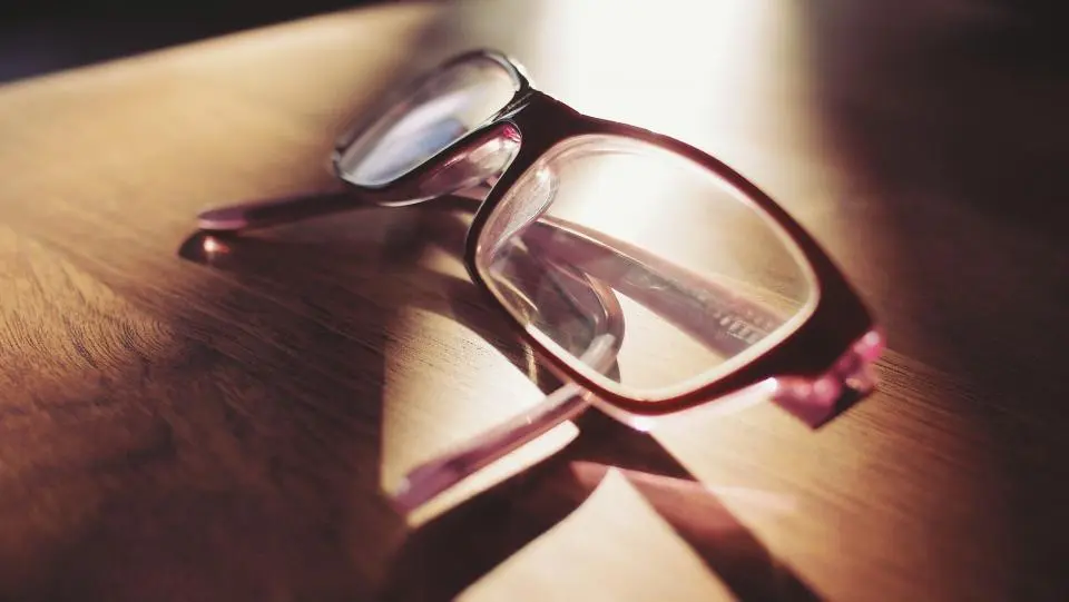 Gafas de montura granate apoyadas en una mesa de madera con luz de tarde