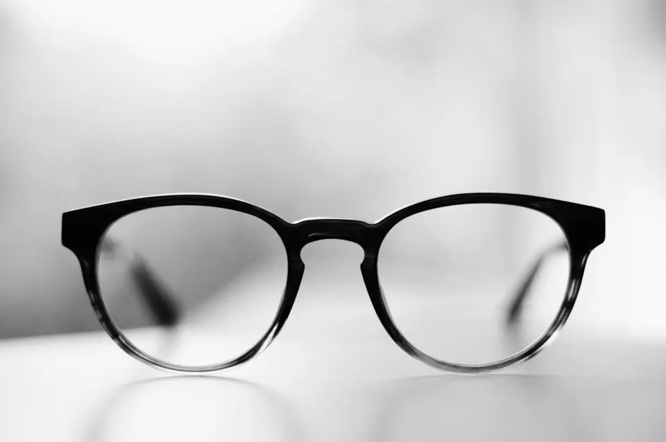 Gafas de montura redonda negra apoyadas sobre una mesa blanca