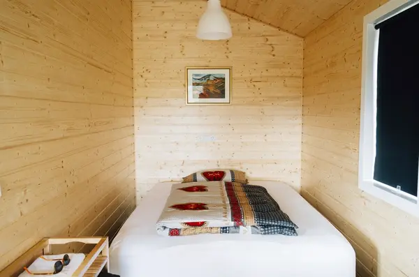Habitación pequeña revestida de madera con cama y colcha de cuadros.