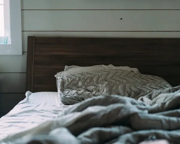 Cama con colcha de lana gris junto a una pared de madera.
